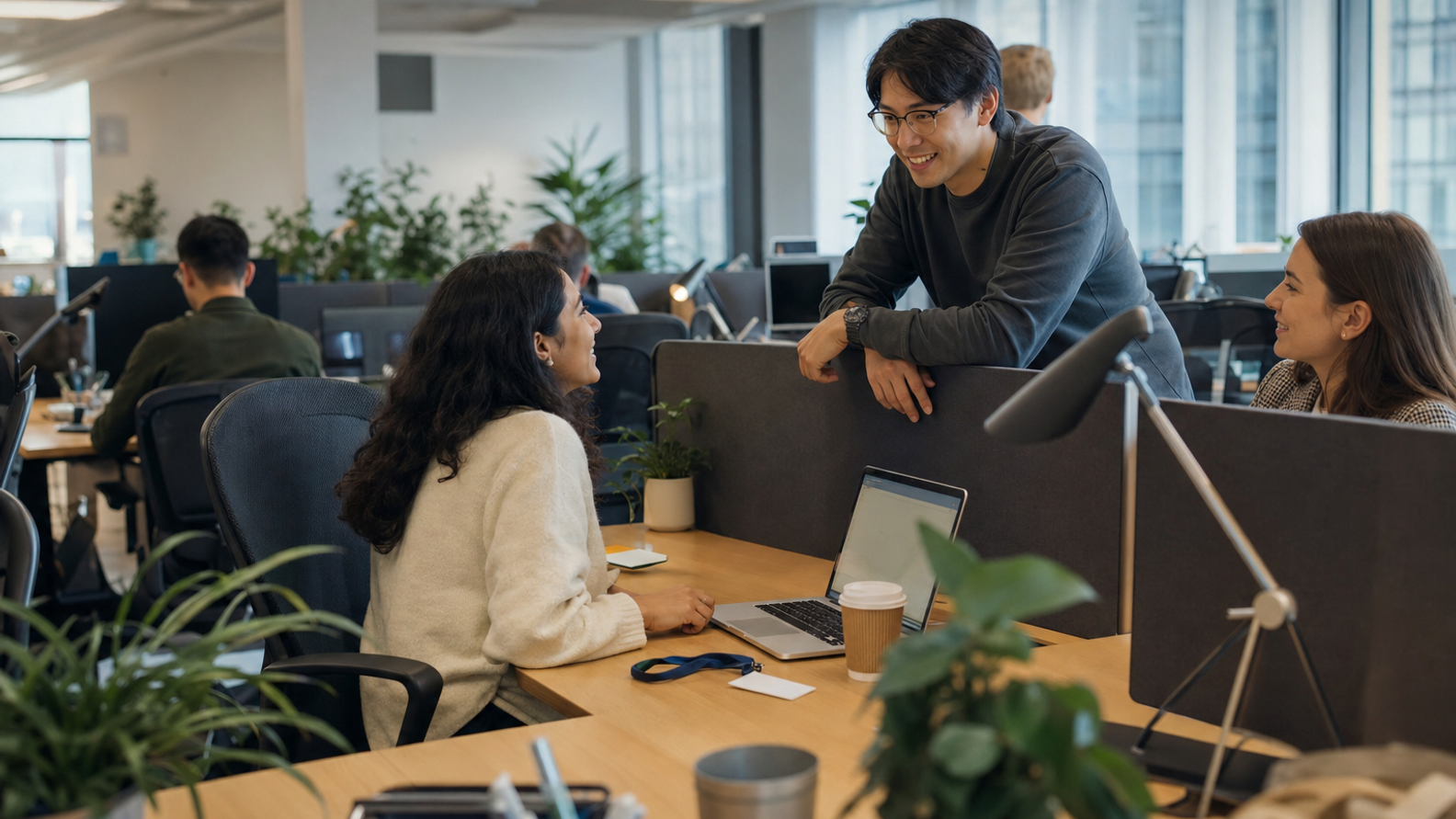 A new colleague sitting down at a previously empty desk on their first morning while a team-mate leans in to say hello